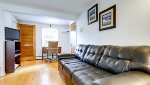 Un salon avec un canapé en cuir, un parquet, un téléviseur posé sur un meuble, un bureau avec une chaise et deux tableaux encadrés accrochés au mur.