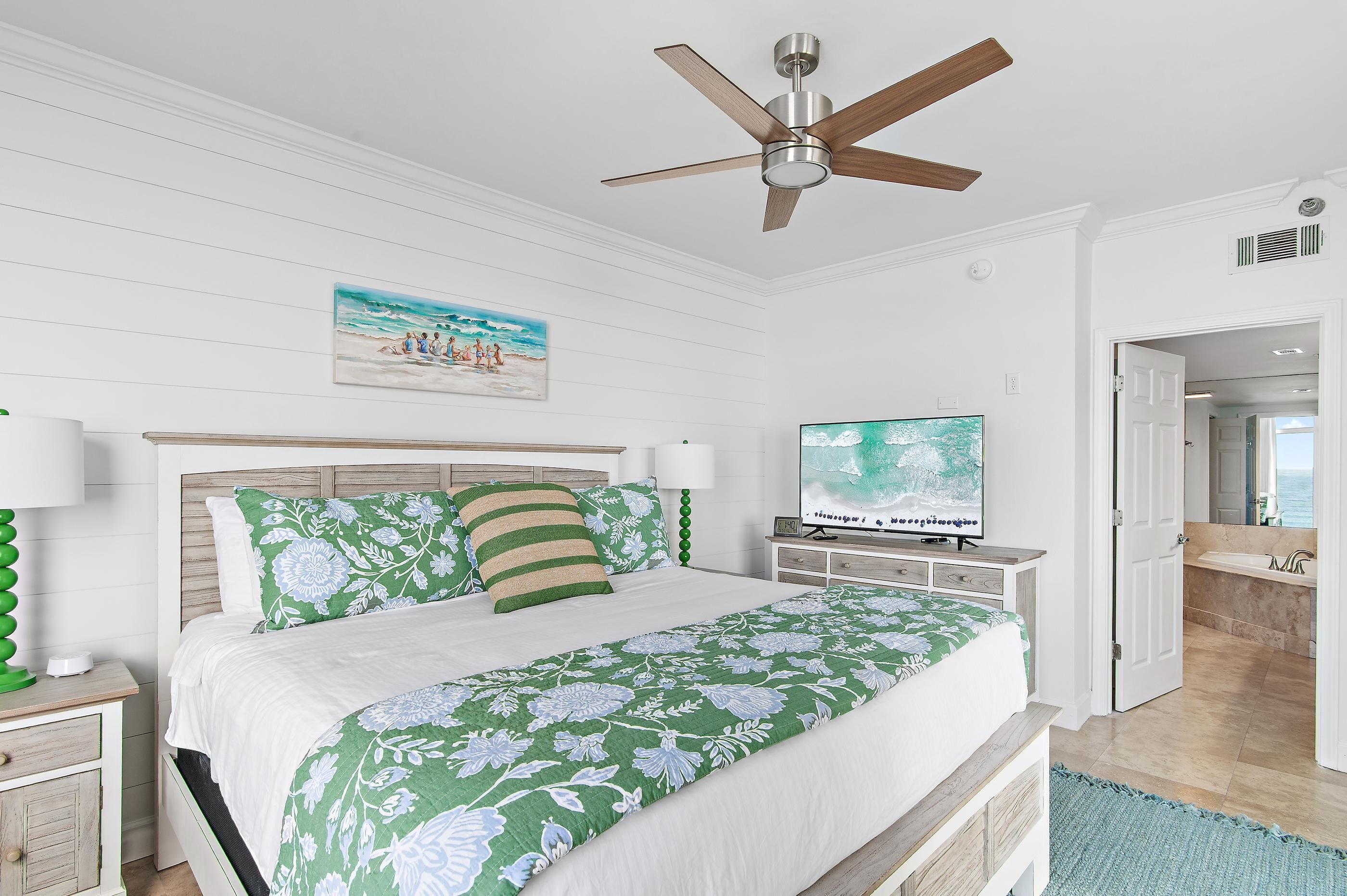 Une chambre à coucher avec un lit, un ventilateur de plafond, une télévision et un tableau au mur.