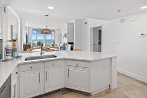 A modern kitchen with white cabinetry, a large island, and a view to the outside. - Jade East 510- Grand Escape (Destin)