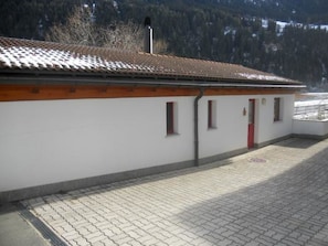 A building with a tiled roof, a red door, and a paved ground.