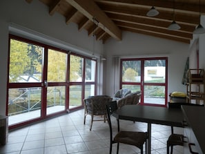 A room with large windows, a dining table, chairs, and a wooden ceiling. - Baeder, (Müstair) by Interhome (Müstair)