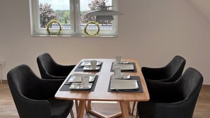 Zona pranzo con tavolo imbandito per quattro, sedie nere, lampadario e finestra con persiane.