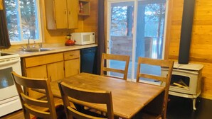 A wooden dining table with chairs, a microwave, a stove, and a wood-burning stove. - Blue Moon Retreat (Combermere)