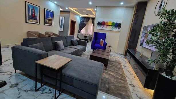 A modern living room with a sofa, armchair, coffee table, and a TV. - Bayford Suites (Abuja)