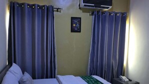 A hotel room with a bed, curtains, an air conditioning unit, a bedside table with a phone, and a motivational quote on the wall. - Bayford Suites (Abuja)