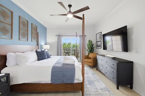 Un dormitorio con cama, ventilador de techo, cómoda, televisor y balcón con vistas.