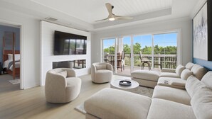 A spacious living room with a ceiling fan, a flat-screen TV mounted on the wall, a large sofa, and a balcony with outdoor furniture. - New! Epic Cabana Court Luxe Retreat (Kissimmee)
