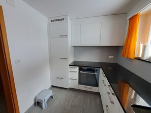 A compact kitchen with white cabinets, a built-in oven, and a small stool.