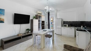 A modern kitchen with white cabinets, a dining table with chairs, a TV mounted on the wall, and a ceiling fan. - Apartment 'Mirosa' with Balcony, Wi-Fi and Air Conditioning (Pompei)