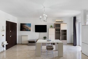 Een moderne keuken met een eettafel, stoelen, een kroonluchter, een televisie en een radiator.