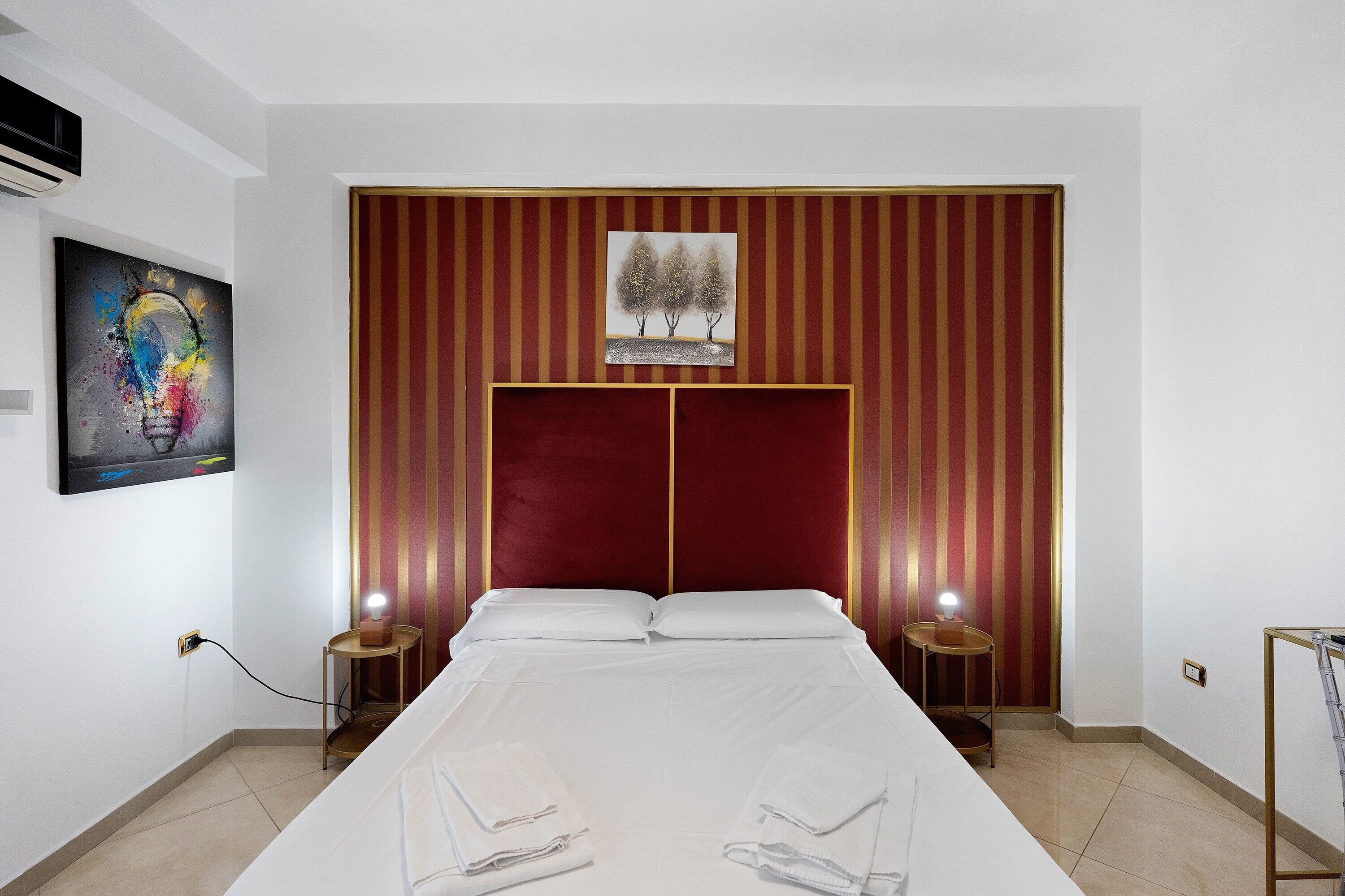Hotelkamer met een groot bed, twee nachtkastjes, een rode hoofdbord, een schilderij aan de muur en een klein tafeltje met een lamp.