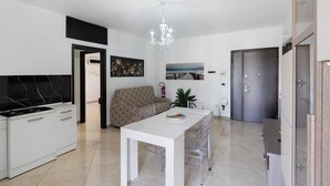 A modern kitchen with white cabinets, a black marble backsplash, a dining table with chairs, a chandelier, and a sofa. - Apartment 'Mirosa' with Balcony, Wi-Fi and Air Conditioning (Pompei)