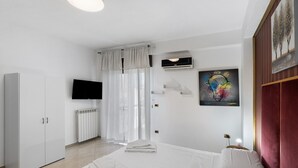 A hotel room with a bed, a wardrobe, a television, a radiator, and a painting on the wall. - Apartment 'Mirosa' with Balcony, Wi-Fi and Air Conditioning (Pompei)