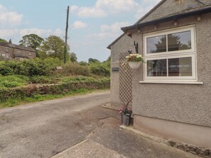 A building with a stone facade, a window with a white frame, and a hanging flower basket. - Little Plumtree (Milnthorpe)