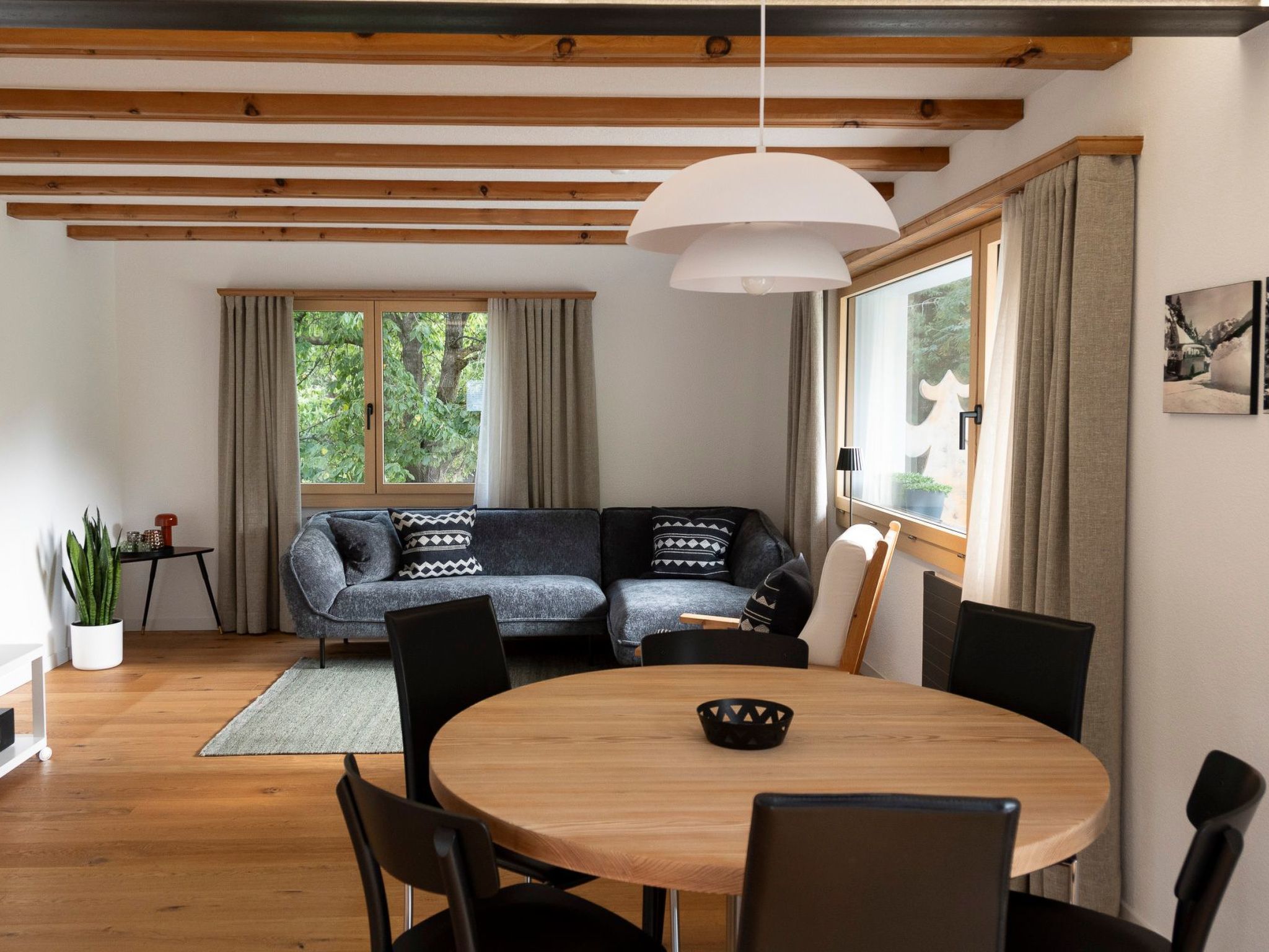 A modern living room with a wooden ceiling, a round dining table, and a grey sofa with patterned cushions.