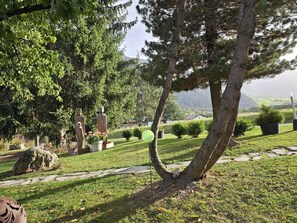 A landscaped garden with a variety of trees, a stone pathway, and a view of a distant landscape. - Schaivel, (Müstair) by Interhome (Müstair)