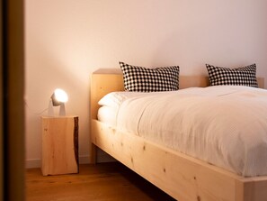 A bed with a wooden headboard, two checkered pillows, and a bedside lamp on a wooden nightstand. - Schaivel, (Müstair) by Interhome (Müstair)