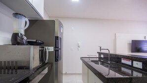 Een keuken met een blender, magnetron, koelkast, spoelbak en een flatscreen televisie aan de muur.