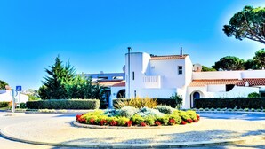 Un bâtiment blanc surmonté d’un toit recouvert de tuiles rouges, entouré d’un jardin aménagé avec des fleurs rouges et divers arbustes.