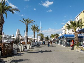 Eine Küstenpromenade mit Palmen, Sitzgelegenheiten im Freien und einem sichtbaren Deck-Loungesbereich.