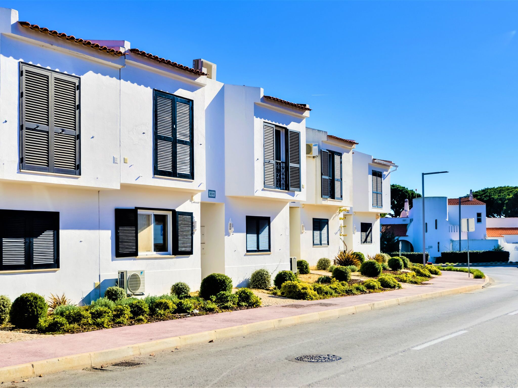 A row of white buildings with black shutters, a clear sky, and a paved road.