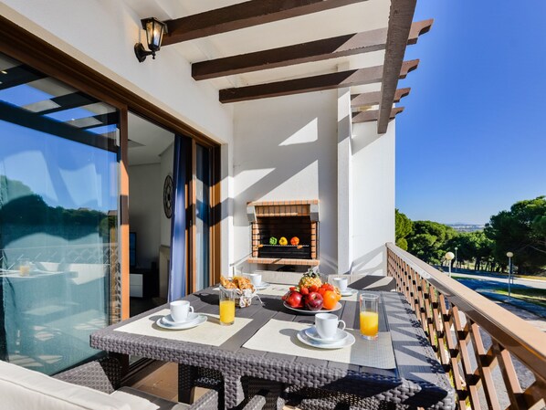 Un balcón con una mesa preparada para el desayuno, una parrilla y vistas a una piscina.
