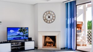 A modern living room with a flat-screen TV, a fireplace, and a large wall clock. - Apartment  by Interhome (Albufeira)