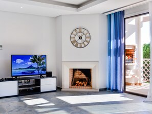 A modern living room with a flat-screen TV, a fireplace, and a large wall clock. - Apartment  by Interhome (Albufeira)