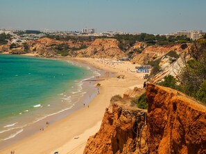 A coastal beach with clear turquoise water, sandy shores, and rocky cliffs. - Apartment  by Interhome (Albufeira)