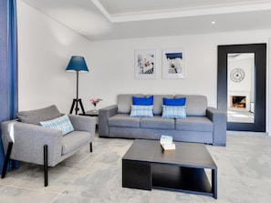 A modern living room with a grey sofa, a grey armchair, and a black coffee table. There are two blue pillows on the sofa and a blue floor lamp. - Falesia Beach A by Interhome (Albufeira)