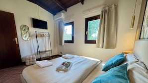 Een slaapkamer met een bed, kussens, een nachtkastje, een raam en een deur.