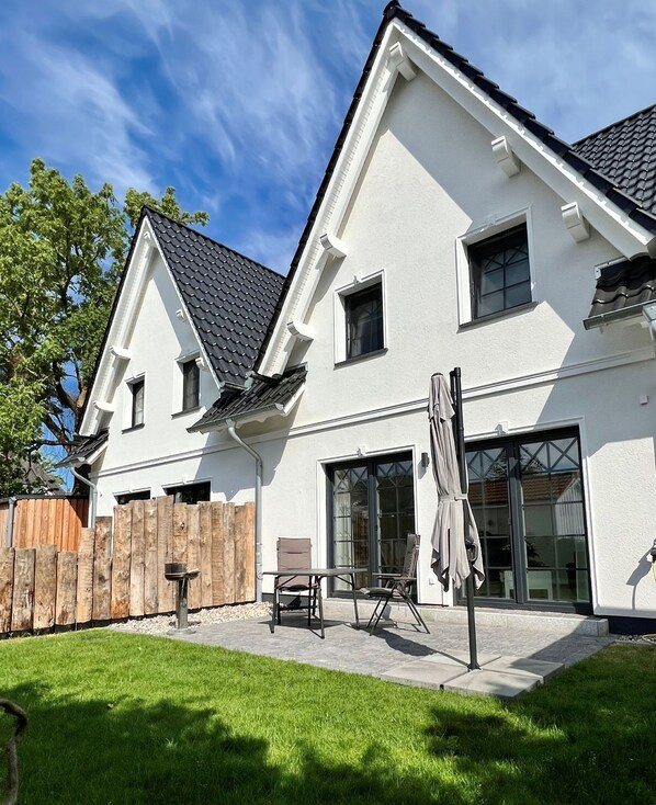 A two-story house with a white exterior, a dark roof, and a fenced backyard.