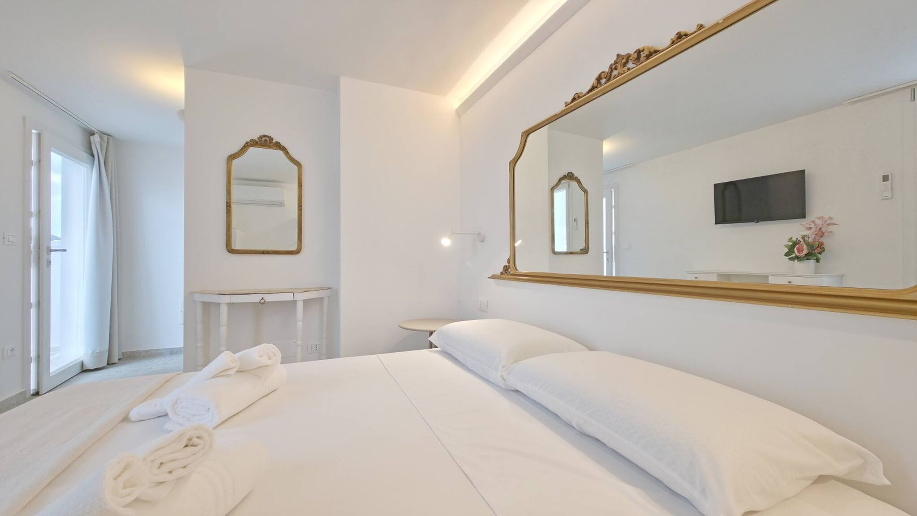 Une chambre d’hôtel avec un lit, un grand miroir, une télévision et une fenêtre avec des rideaux.