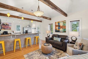 A modern kitchen with bar stools, a leather sofa, and abstract art on the walls. - Yew 2!- House + Carriage House- Steps to Beach! (Santa Rosa Beach)