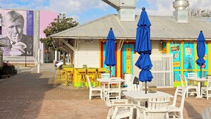 Un espace extérieur aménagé avec des tables et des chaises, un bâtiment doté d’une enseigne colorée et une fresque murale.