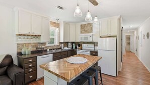 Une cuisine moderne avec des meubles blancs, un îlot central en bois, des tabourets de bar et des luminaires suspendus.