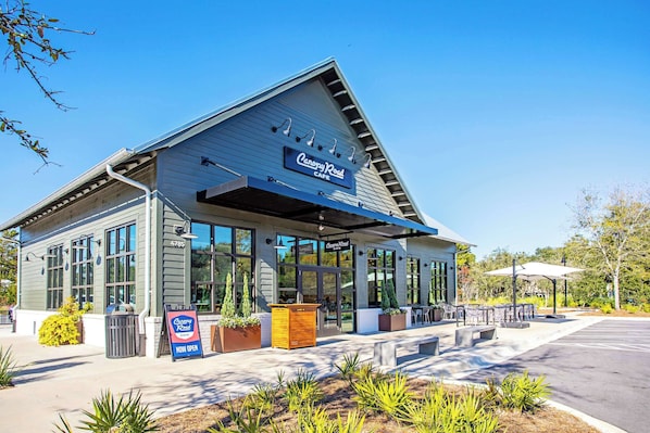 A Canopy Road Cafe with a modern design, large windows, outdoor seating, and a clear sky.