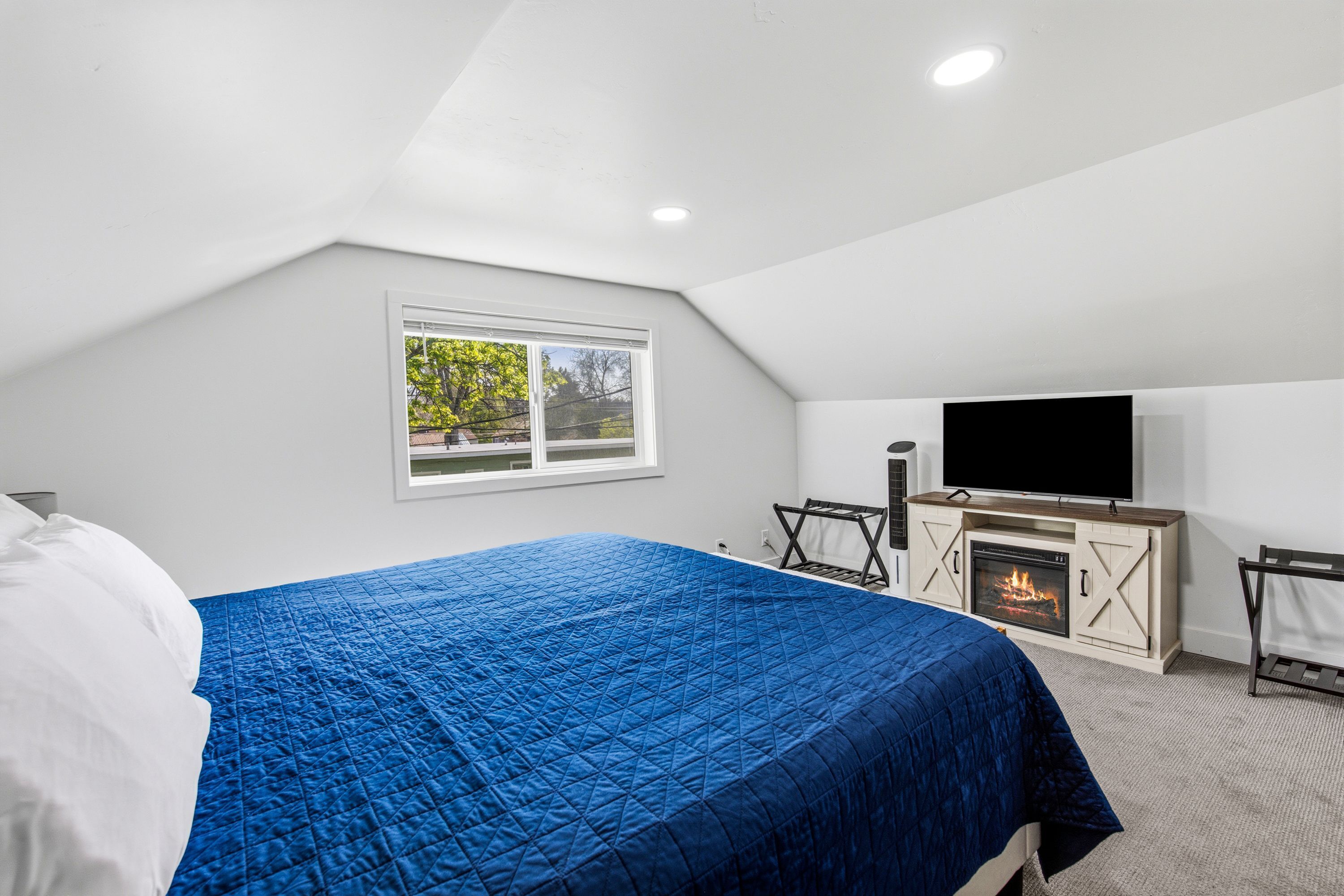 A bedroom with a bed, a television, a fireplace, and a window.