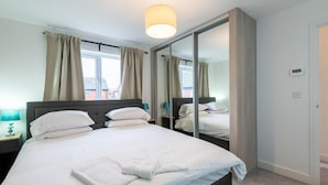 Ein Schlafzimmer mit einem großen Bett, einem Nachttisch mit Lampe, einem Spiegel und Blick ins Freie.