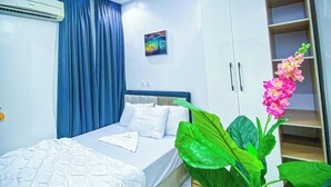 A bedroom with a bed, a ceiling light, an air conditioning unit, a painting, and a plant. - Jay's Wood Hotel And Apartment (Benin City)