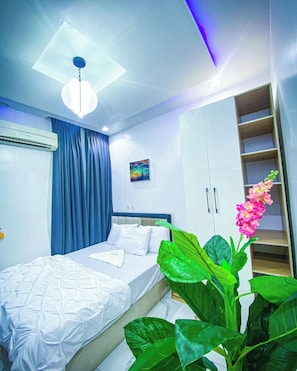 A bedroom with a bed, a ceiling light, an air conditioning unit, a painting, and a plant. - Jay's Wood Hotel And Apartment (Benin City)