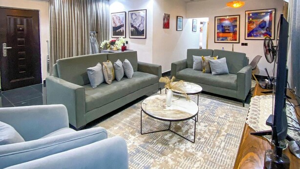 A modern living room with grey sofas, a coffee table, and a TV stand. - Jay's Wood Hotel And Apartment (Benin City)