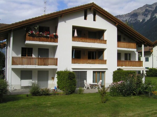 A multi-story hotel with balconies, a covered outdoor seating area, and a mountainous backdrop.