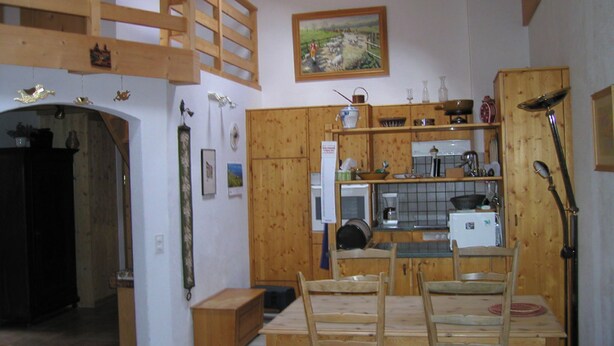 A rustic kitchen with wooden cabinets, a dining table with chairs, and a painting on the wall.