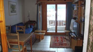 A living room with a sofa, chairs, a dining table, a TV, and a balcony with a railing.