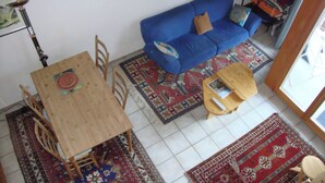 A room with a wooden dining table, a blue sofa, and patterned rugs.
