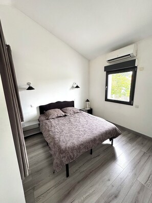 Ein Schlafzimmer mit einem Bett, zwei Nachttischlampen, einem Fenster und einer Klimaanlage.
