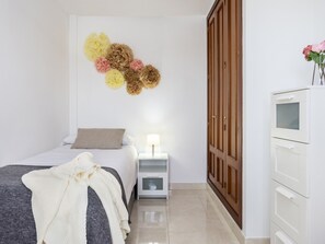 Une chambre à coucher avec un lit, une table de chevet, une lampe, une armoire et des fleurs décoratives accrochées au mur.