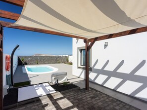 Un espace extérieur abrité comprenant une piscine, un mur en pierre et une vue sur la mer.