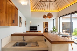 Eine moderne Küche mit eingebautem Spülbecken, Holzschränken, einem Flachbildfernseher und einem Essbereich mit Blick.